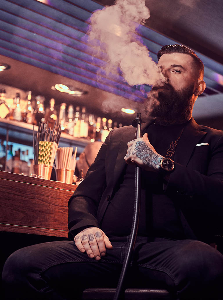 tabacaria_0001_portrait-tattooed-bearded-man-which-is-smoking-hookah-making-nice-vapour-while-sitting-near-bar-counter